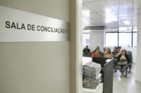 Porta da Sala de Conciliação entreaberta, ao fundo grupo de pessoas sentadas na espera