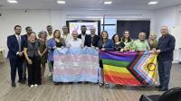 Várias pessoas reunidas. Elas seguram bandeiras coloridas simbolizando o movimento LGBTQIAP+