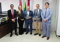 Foto de cinco pessoas de pé, sorridentes, um deles, o desembargador Marcelo Vieira, ao centro, segurando um livro
