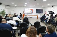 Mulher loira na frente de um grupo de pessoas sentadas apresentando um slide