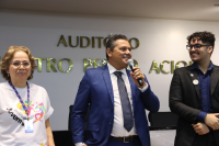 Há três pessoas na foto, sendo uma mulher de pele clara vestida de roupa branca e dois homens vestidos de ternos em tons escuros,