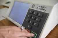 Urna eletrônica. Há uma mão feminina clicando em uma tecla verde.