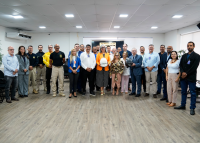 Várias pessoas reunidas para uma foto. Há uma mulher e um homem segurandao capacetes de motociclista.