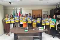 Grupo de homens e mulheres em trajes formais segurando um cartaz amarelo com o dizer Prêmio Trabalho Seguro