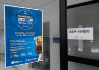 À esquerda, cartaz azul com letras brancas e douradas. Em destaque no cartaz, o nome Execução Trabalhista escrito em letras brancas; à direita, uma porta de vidro com o nome bem-vindo escrito em letra azul