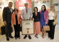 Grupo de homens de terno e mulheres de trajes sociais segurando um quadro com diploma