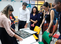 Várias pessoas reunidas em torno de uma mesa. Elas olham para um notebook