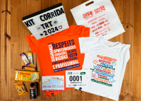 Há um kit de coorida, composto por duas camisetas, sendo uma na cor laranja e outra na cor branca,. Também tem sacola, biscoitos, chocolates.