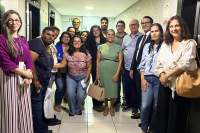 17 pessoas em pé, entre homens e mulheres; ao centro do lado direito, a juíza Luciana Espírito Santo, que é uma mulher de pele morena, de cabelo preto preso e usando  vestido verde.