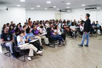 Home moreno, alto, magro, de blazer preto, em pé; frente dele, vários estudantes sentados escutando a sua palestra