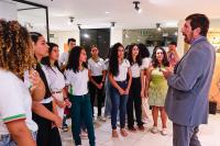 Vários estudantes reunidos. Eles estão de frente a um homem que fala para eles. O homem  que é branco veste terno cinza.