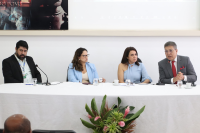 Dois homens de terno e duas mulheres vestindo azul sentado em uma mesa com uma toalha branca e um arranjo ao centro