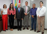 Seis pessoas posam para foto. Sendo duas mulheres vestidas com  calças comprida e blusas coloridas. Dos quatro homens, há dois que estão de terno e dois de camisa de manga comrpridas.
