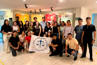 Várias pessoas reunidadas parauma foto. Umas estão de pé e há outras agachadas. Elas seguram uma bandeira com uma logomarca.