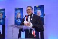 Homem alto, moreno, de cabelo grisalho, toga preta, discursando atrás de um púlpito transparente