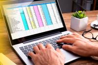 Há um notebook com a tela aberta, no qual há mãos brancas digitando no teclado.