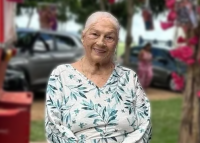 Mulher idosa de cabelo branco presos sorrindo, vestindo uma camisa verde