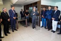Vários homens em pé,  vestidos de ternos escuros. Há apenas uma mulher de roupa preta atrás de um homem que fala ao microfone.