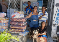 Há dois homens e duas mulheres. Eles estão ao lado de vários sacos de alimentos. Uma das mulheres está abaixada e tem tem um cachorro a seu lado.