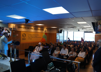 foto de um auditório com várias pessoas e um homem de terno branco à frente falando
