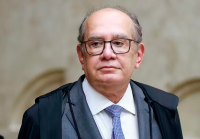 Homem branco de óculos preto, calvo, de terno cinza e toga preta