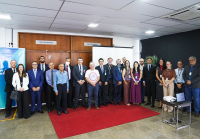 A imagem mostra um grupo de magistrados, servidores e representantes da Caixa Econômica Federal reunidos em frente à sala de sessões do TRT da 19ª Região, durante encontro institucional. Os participantes posam para a foto sobre um tapete vermelho, evidenciando o clima de integração e parceria entre as instituições.