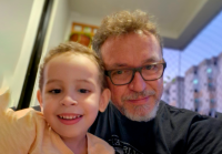 Há uma criança ao lado deum um adultos. Eles são de pele branca. O homem usa óculos.