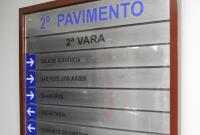 A imagem mostra uma placa de sinalização interna em uma parede, indicando os ambientes do 2º pavimento de um prédio, mais especificamente da 2ª Vara. A placa tem moldura de madeira escura e fundo prateado com letras em azul e preto.
