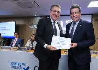 Dois homens altos grisalhos usando ternos escuros, gravatas cinzas escuras em pé segurando um diploma branco