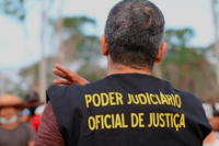 Foto de um oficial de justiça de costas com o jaleco preto com o nome poder judiciário oficial de justiça escrito em letras amarelas