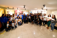 Grupo de estudantes e adultos posa sorrindo.Há no local, painéis informativos ao fundo. Estão em um ambiente interno iluminado, com piso branco e clima de visita educativa.