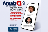 Ao lado direito, um aparelho de celular com as imagens de um homem moreno no alto e um homem branco embaixo da referida foto, ao lado esquerdo, o nome Amatra 19 na parte superior esquerda.
