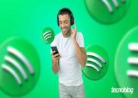 Imagem com fundo verde e quatro símbolos do spotify; ao centro, um homem jovem magro de cabelos pretos usando calça cinza e camiseta branca, segurando o telefone celular preto com a mão direita.