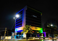 Imagem noturna de um prédio de oito andares iluminado com as cores do arco-íris em homenagem ao público LGBTQIA+