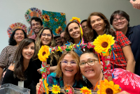 Foto de onze pessoas, sendo mulheres e quatro homens, sendo as mulheres vestidas de roupas juninas e com ornamentos nas mãos.