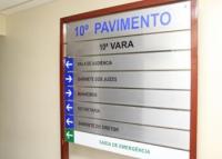 Placa cinza com nomes em sentido vertical escritos em preto. acima centralizado, o nome 10ª Pavimento escrito em letras azuis e abaixo dele o nome 10ª Vara escrito em letras pretas