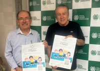 Dois homens idosos segurando um cartaz grande; um homem usa camisa social azul clara e o outro camiseta preta