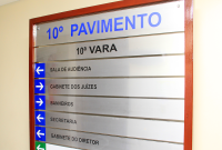 PLACA DE PVC NA COR CINZA ESCURO,  COM O NOME 10ª VARA DO TRABALHO DE MACEIÓ ESCRITO EM LETRAS PRETAS; ABAIXO DELE, DE CIMA PARA BAIXO, OS NOMES SALA DE AUDIÊNCIA, GABINETE DOS JUÍZES, BANHEIROS E SECRETARIA, TODOS NA COR PRETA. 