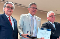 Três homens, sendo dois de terno escuro e um de terno claro segurando um certificado