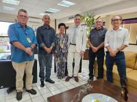 Na foto, cinco homens e uma mulher posado para a foto. Todos me pé olhando para a frente; a mulher usa macacão verde com estampas brancas e pretas