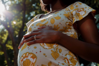 Foto com foco na barriga de uma mulher negra grávida usando vestido estampando em branco e amarelo