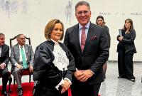 À esquerda, mulher branca e baixa vestindo toga preta; à direita, homem alto e de cabelos parcialmente grisalho vestindo terno preto. Ambos estão em pé em pose para a foto