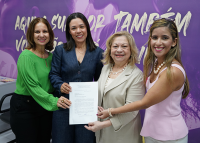 Há quatro mulheres segurando um papel. Elas estão sorridentes e posando para a foto