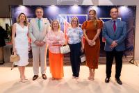Seis pessoas em pé posadas para a foto, sendo quatro mulheres e dois homens que usam terno. Todos estão com roupas formais