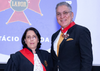 Mulher branca baixo de cabelo preto  e toga preta à esquerda; à direita, homem alto de toga preta e cabelos grisalho. Os dois estão usando óculos