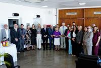 Várias pessoas reunidas para fotos. Els estão sorridentes. A maioria dos homens veste terno nas cores claras e escuras.. 