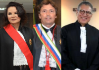 Um mulher de cabelos pretos e toga preta com faixa vermelha, um homem branco com faixa de vermelha, azul e branca e homem de oculos e toga preta