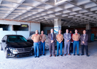 Carro sedan preto e ao lado dele sete homens bem vestidos, sendo três usando paletó e quatro usando farde do corpo de bombeiros