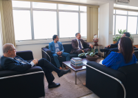Há quatro homens vistidos de ternos e uma mulher de roupa azul. Eles estão sentados conversando.