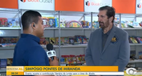 Há dois homens, sendo um de camisa azul com um microfobe na mão e e ontro de terno cinza claro.